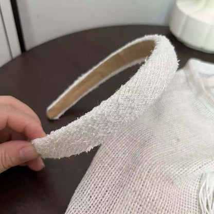 A single cream boucle textured headband held by hand on a dark wood table.