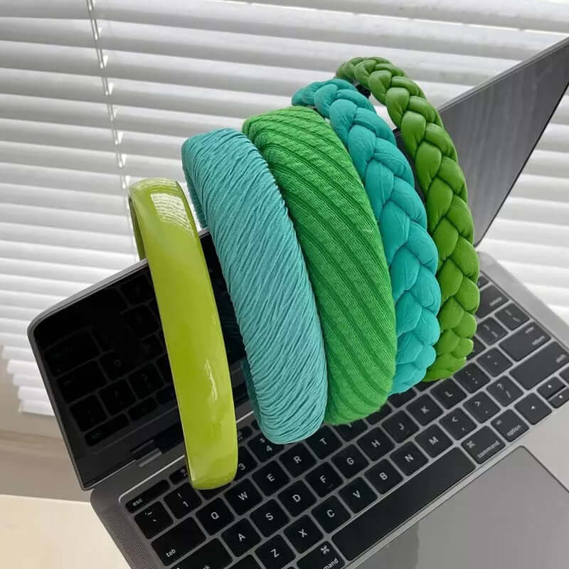 Five green and teal headbands in patent, ribbed, braided and cable-knit styles, propped on a laptop keyboard - a generic catalog shot.
