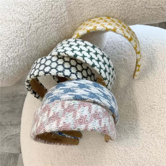 Four padded headbands in mustard, black and white, blue, and pink houndstooth patterns resting on a cream boucle chair.