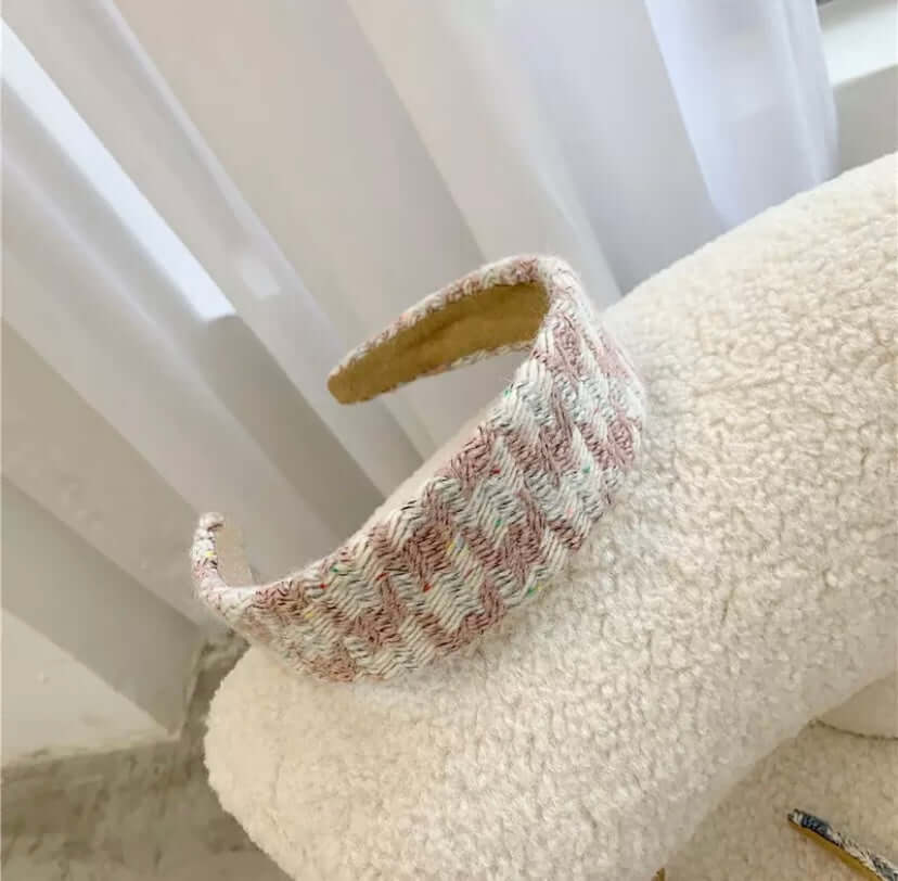 A single pink and cream ribbed striped textured padded headband resting on a cream boucle chair.