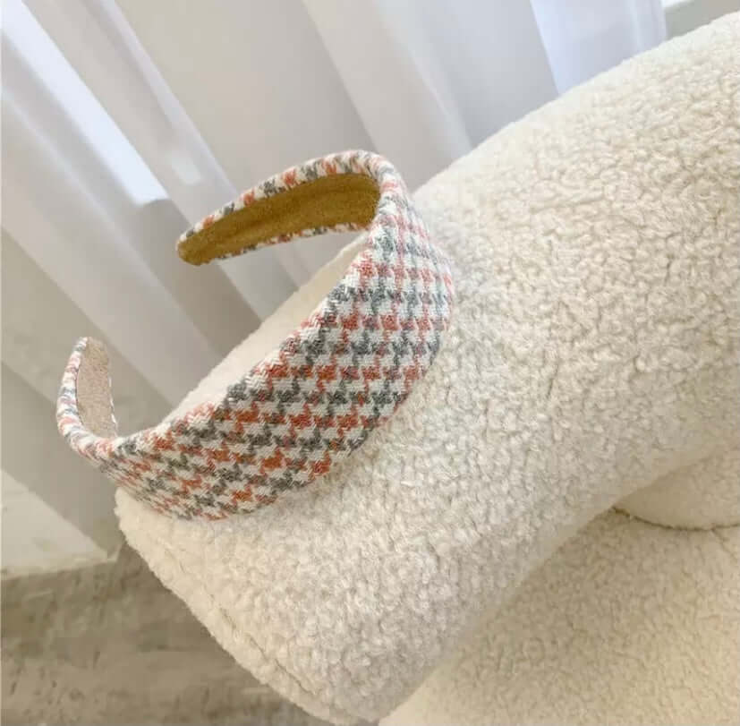 A single coral, grey and cream houndstooth check padded headband resting on a cream boucle chair.