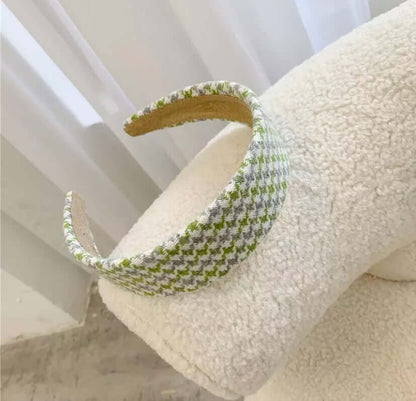 A single green, grey and cream houndstooth check padded headband resting on a cream boucle chair.
