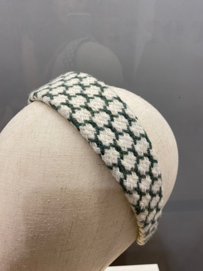 A single dark green and cream houndstooth check padded headband on a mannequin head, studio shot.