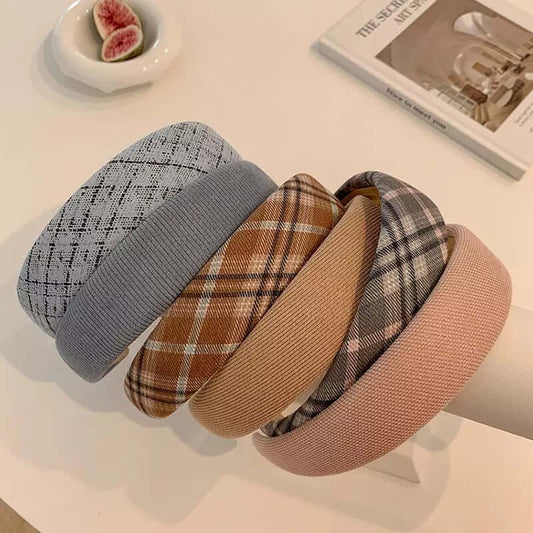 Six different padded headbands - grey tweed, ribbed grey, brown plaid, camel, grey plaid and blush pink - resting together near a dish of figs.