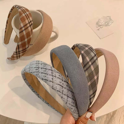 Five padded headbands in brown plaid, camel, grey tweed, ribbed grey and dusty pink patterns held together near a mug and book.