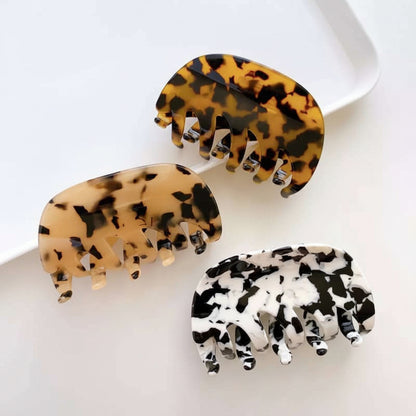 Three acetate hair claw clips - amber tortoiseshell, tan tortoiseshell and black and white mottled - arranged together on a white tray.