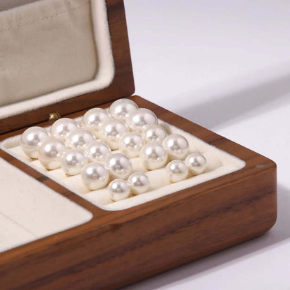 A wooden jewelry box holds multiple pairs of Pearl Me Earrings, showing the full range of pearl sizes.