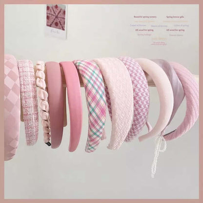 A wide assortment of pink headbands in checkered, tweed, braided, velvet, plaid and quilted styles hanging together as a catalog shot.
