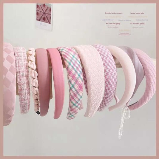 A wide assortment of pink headbands in checkered, tweed, braided, velvet, plaid and quilted styles hanging together as a catalog shot.