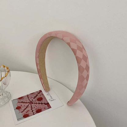 A single pink diamond-quilted patent-look padded headband styled upright near a glass dish and photo card.