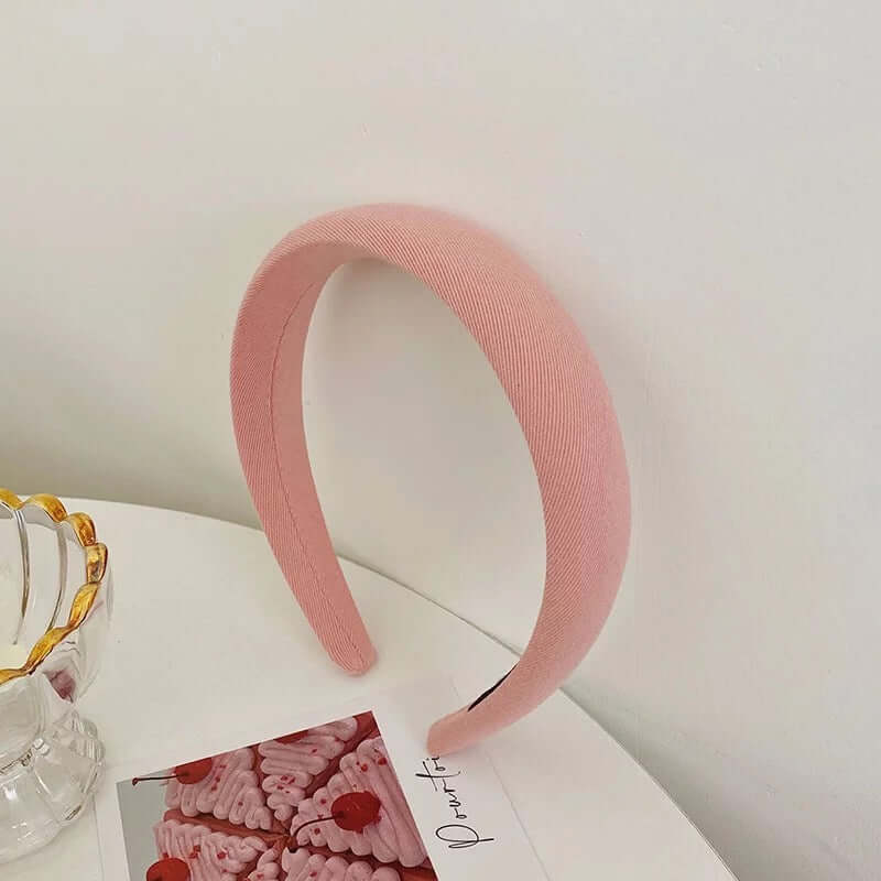 A single pink ribbed twill padded headband styled upright near a glass dish and small photo card.