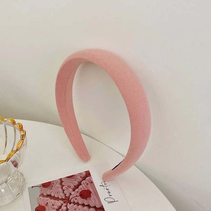 A single pink ribbed twill padded headband styled upright near a glass dish and small photo card.