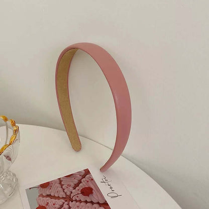 A single solid rose pink glossy padded headband styled upright near a glass dish and small photo card.