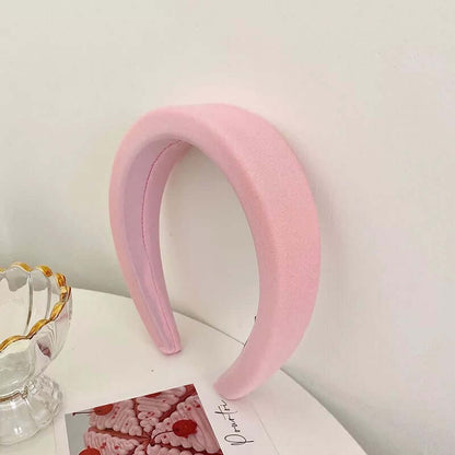A single pink grosgrain-ribbed padded headband styled upright near a glass dish and small photo card.