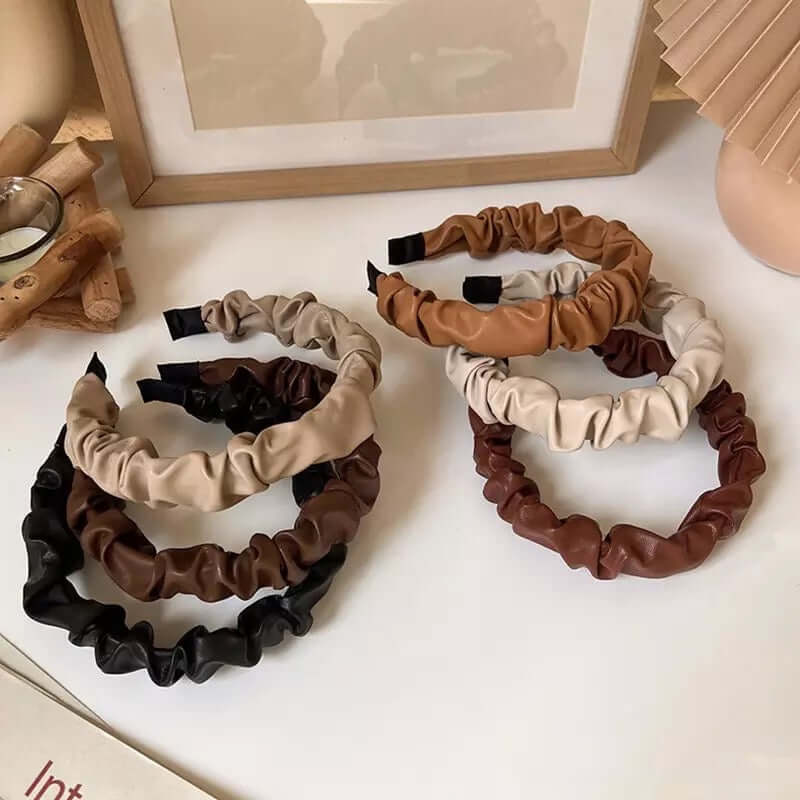 The Romy HAIRBAND set of ruched faux leather headbands in warm neutral tones, styled together with a candle and small wood sticks.