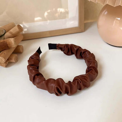 A single dark chestnut brown ruched faux leather Romy HAIRBAND laid flat on a white surface, showing its knotted texture.