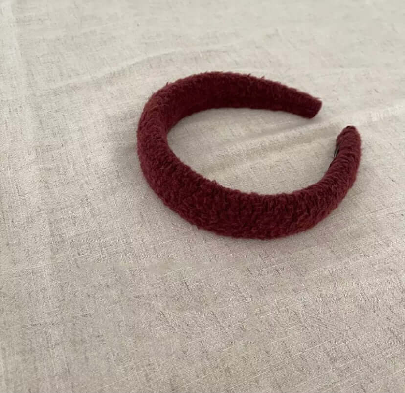 A single burgundy boucle padded Skylar HAIRBAND laid on linen fabric.