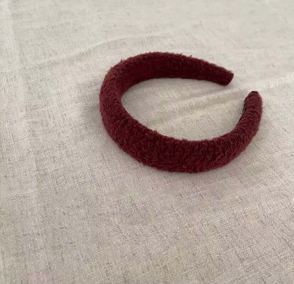 A single burgundy boucle padded Skylar HAIRBAND laid on linen fabric.