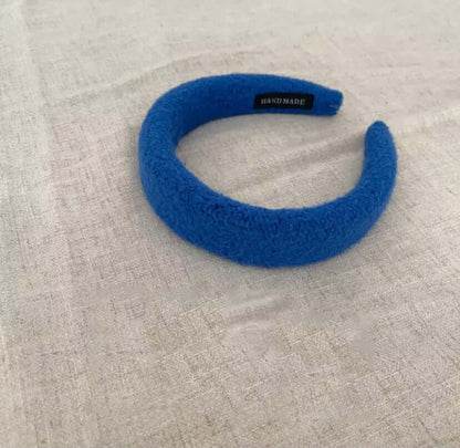 A single cobalt blue boucle padded Skylar HAIRBAND with a handmade label tag, laid on linen fabric.