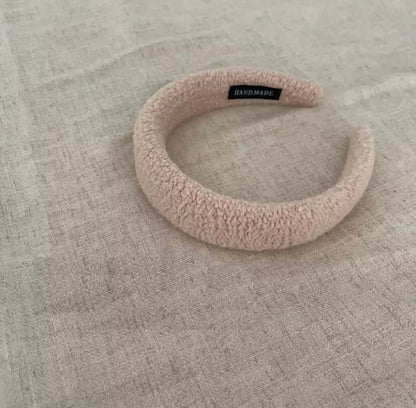 A single blush pink boucle padded Skylar HAIRBAND with a handmade label tag, laid on linen fabric.