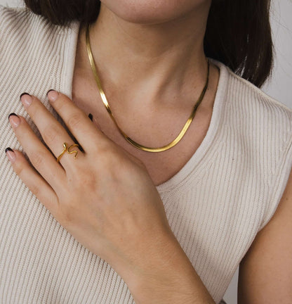 The Snake Skin NECKLACE in gold worn at the neckline over a cream top, paired with a matching snake-shaped ring.