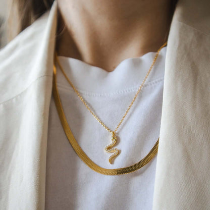 The Snake Skin NECKLACE in gold worn layered with a delicate snake pendant necklace and a herringbone chain over a white tee.