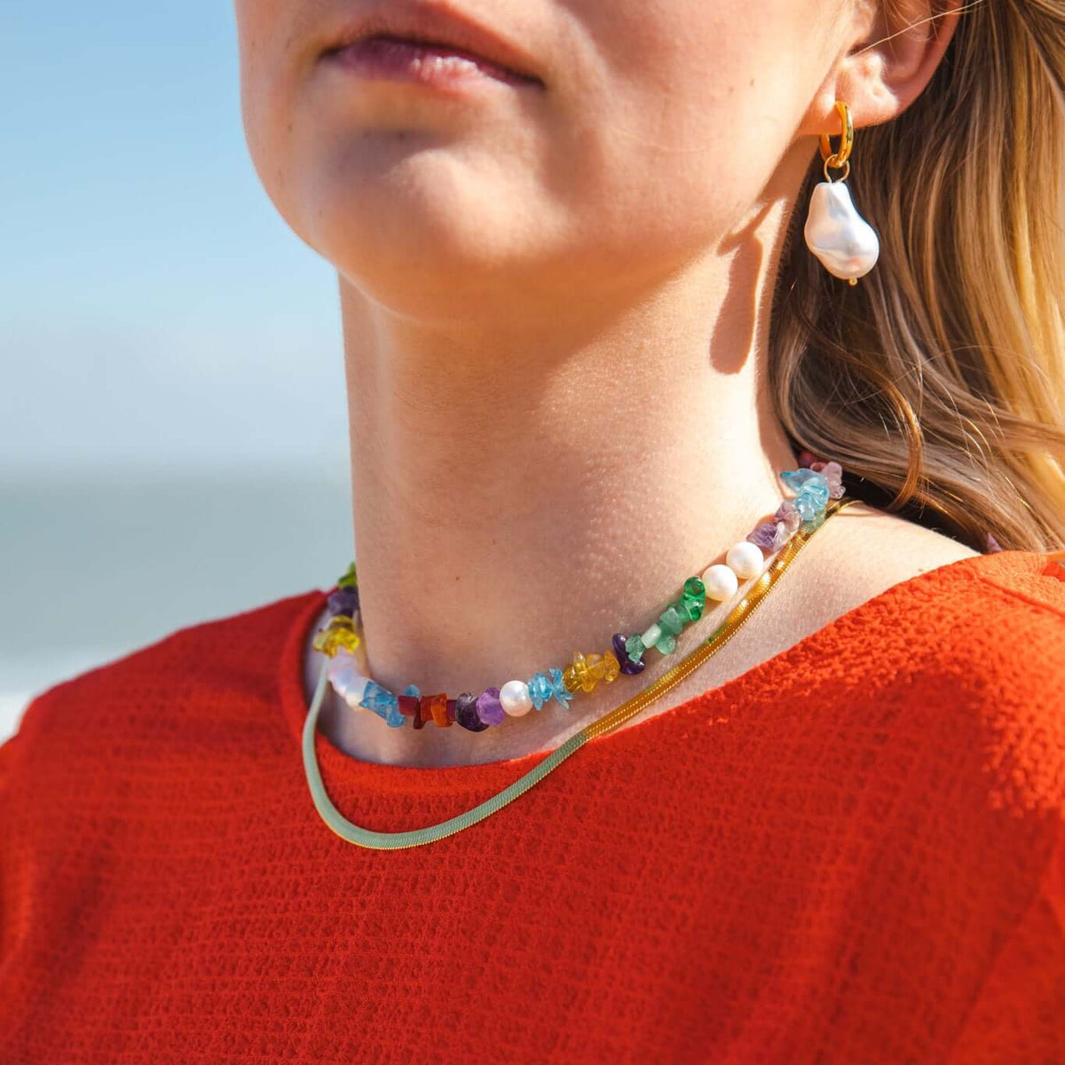 The Snake Skin NECKLACE in gold layered with a multicolor beaded gemstone necklace, worn at the neckline in beach sunlight.