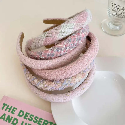 Six pink-toned tweed headbands in different patterns stacked together on a plate near a book.