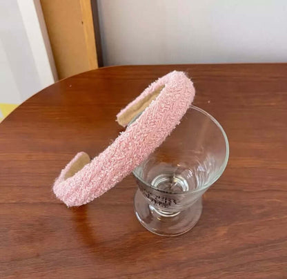 A single solid pink boucle textured headband resting on a wood table beside a glass.