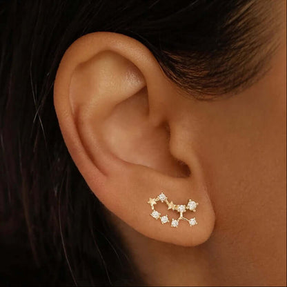 A close-up shows Zodiac Stud Earrings hugging the earlobe, their gold constellation lined with clear stones.